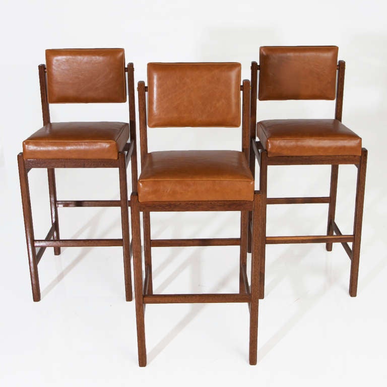 Solid Brazilian Sucupira wood bar stools with wood frame, upholstered seat, pivoting back and patinated brass details. The upholstery is a slightly distressed supple caramel colored or saddle colored leather. 

Price per stool COM/COL is $1850