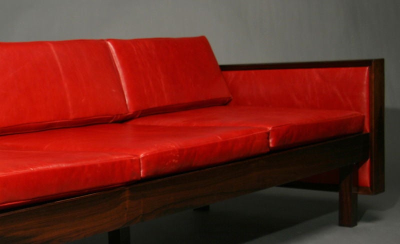 A highly grained rosewood frame sofa upholstered in bright red leather by Fatima Architects, Rio de Janeiro, Brazil. The sides of the sofa are also upholstered and the rosewood shows beautiful sap grain which lends variation to the smooth dark