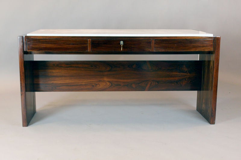 A lovely Rosewood desk designed by Brazil's Joaquim Tenreiro with a thick Carerra marble top and three drawers, one with a new working lock. This desk came from the Bloch, Editores headquarters, a building designed by Oscar Niemeyer and with