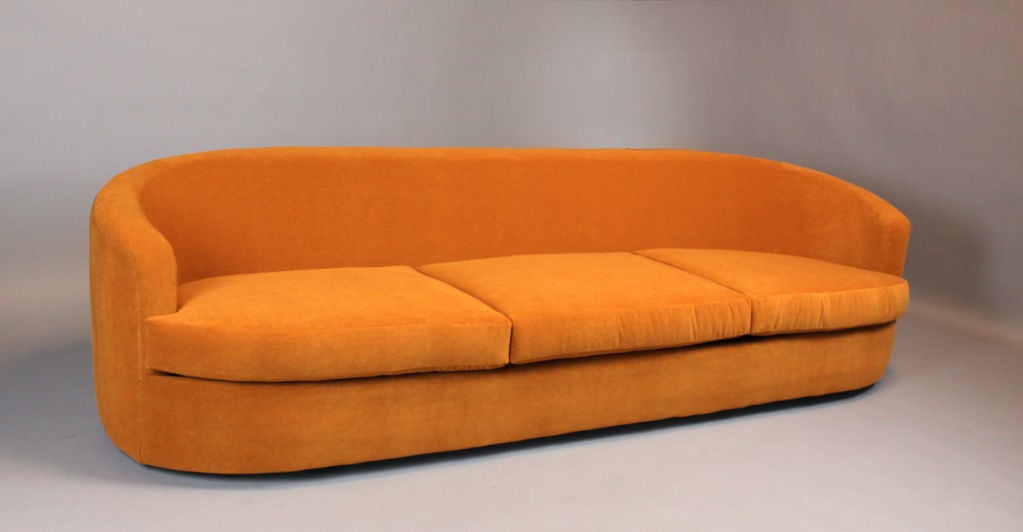 A very comfortable long curved back sofa designed by Milo Baughman and redone in a rich orange mohair. A pair of matching swivel chairs is available.