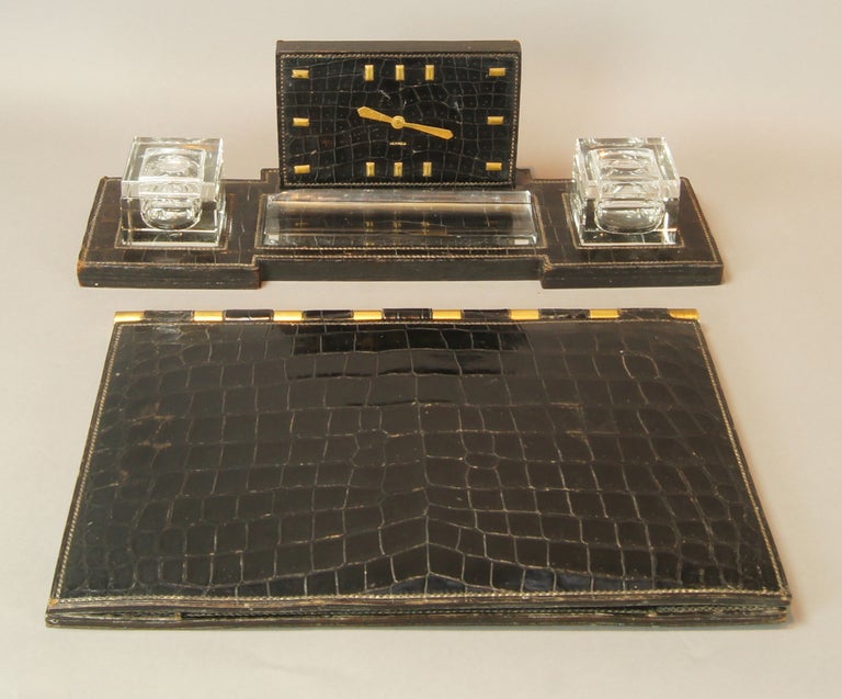 An elegant black crocodile desk set dating from the 1940's consisting of a clock, double ink well and pen tray with matching desk blotter by Hermes. The clock is in perfect working order.