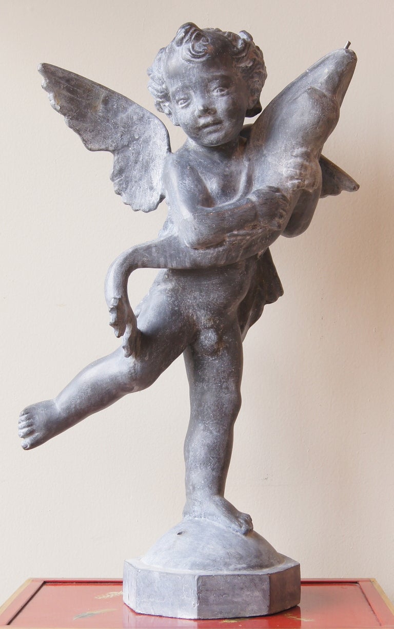 A charming cast lead fountain in the form of a dancing cherub holding a large fish. Water spouts from the fish's mouth.