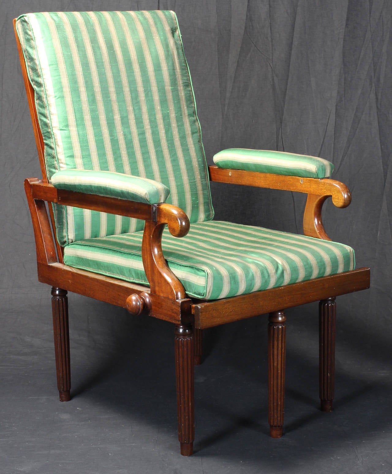 An early 19th century English mahogany Campaign library chair or chaise with caned seat and back and removable cushions. The chair remains in one when folded with the hinged back and arms falling forward against the seat. This is a very efficient