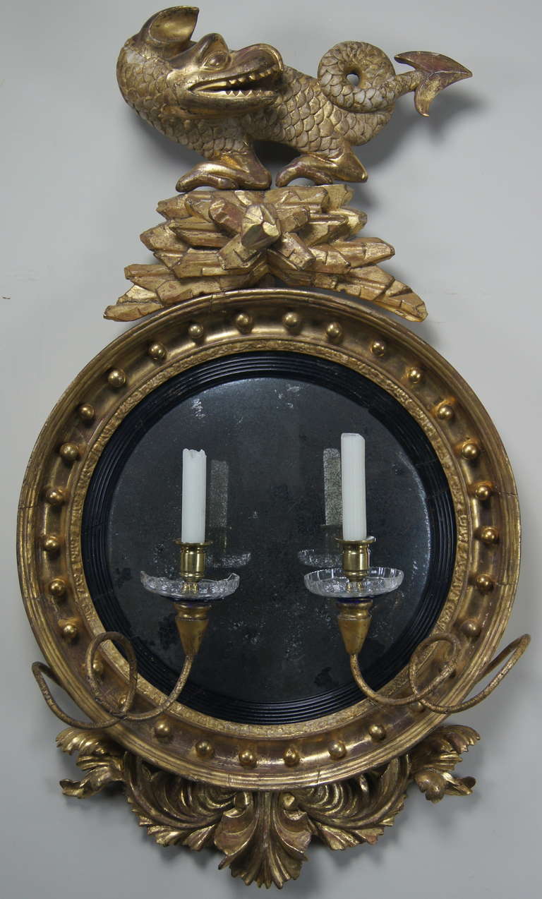 A very fine English Regency convex mirror, the crest with dragon over turned frame with beaded and gilt ball decoration, over foliate carved base.
Regency convex mirrors with dragon crests are scarce.