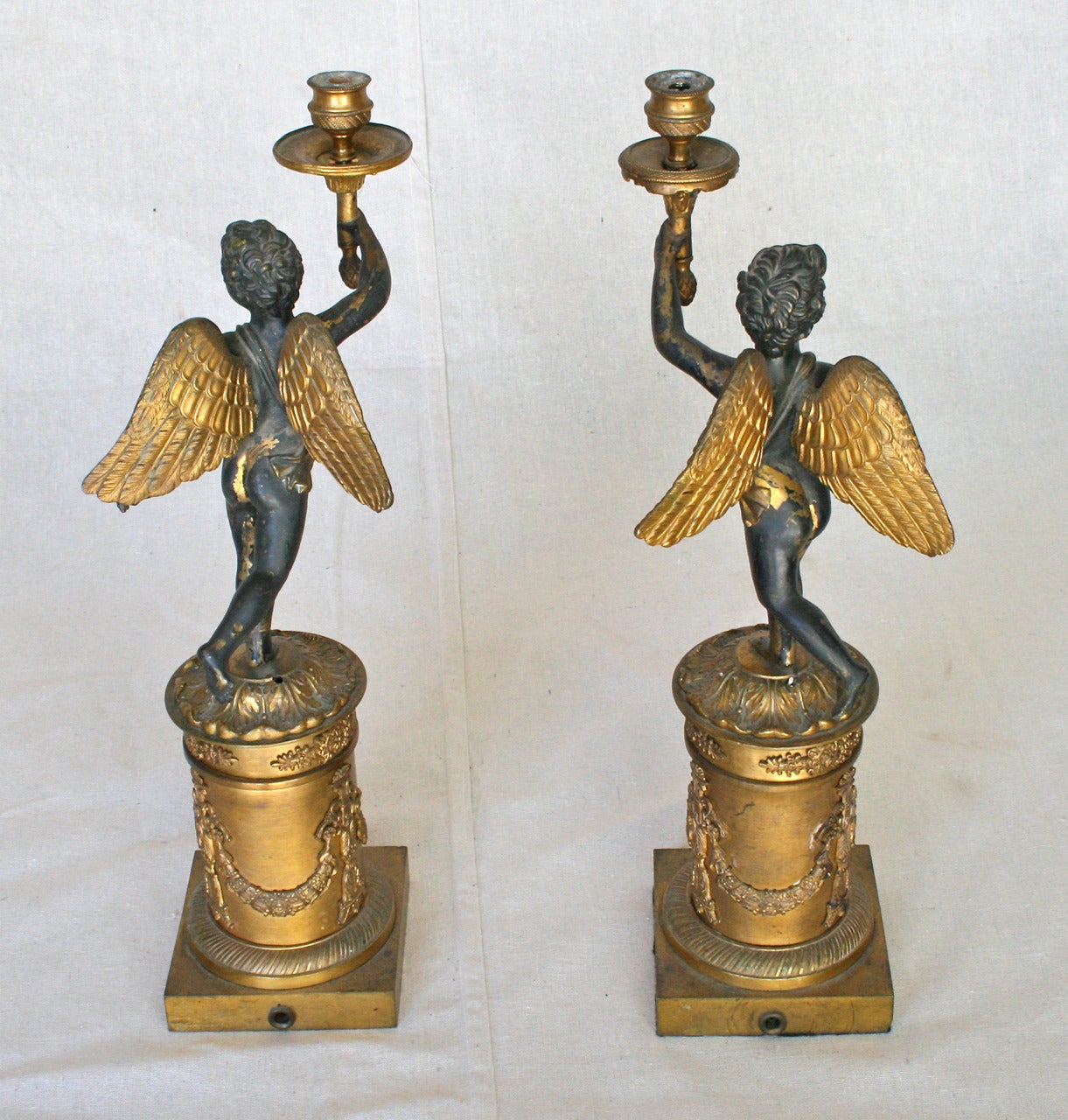 A large pair of late 19th century French Empire style gilt bronze candlesticks depicting winged putti. Each charming cherub is unique from the other.