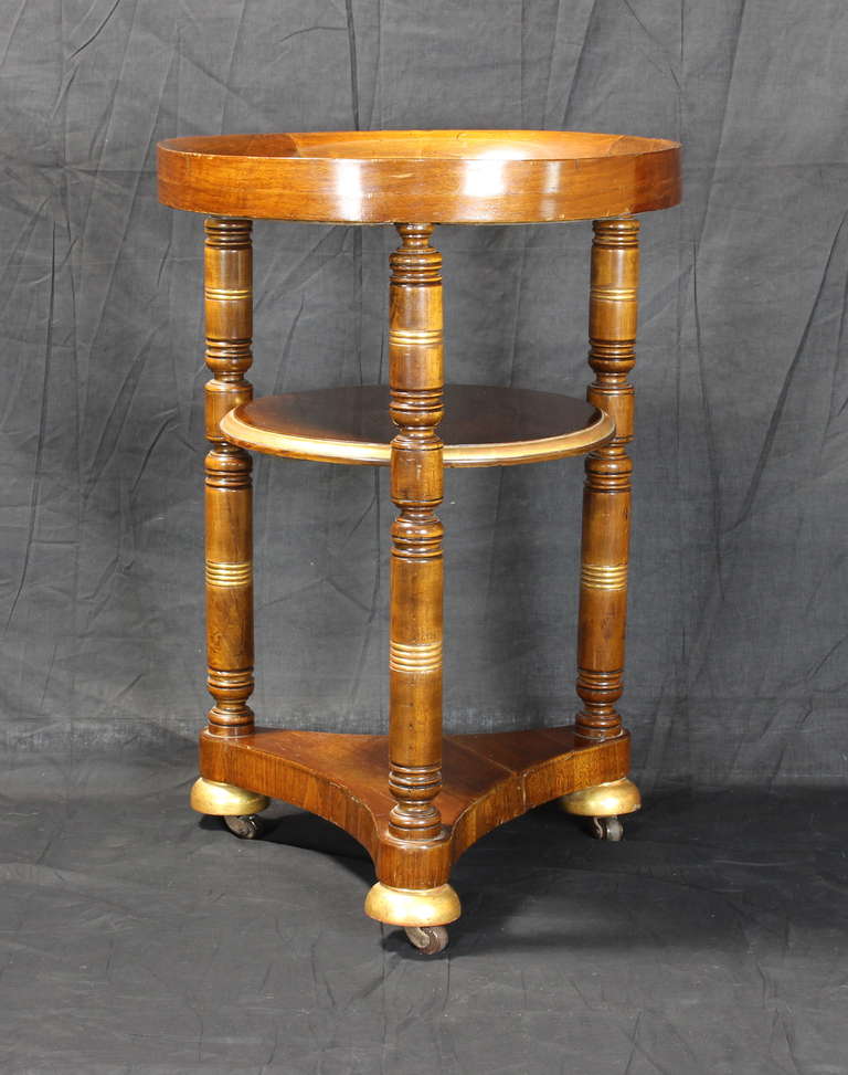 An unusual 19th century mahogany drinks table with water-gilt accents and inset slate top, the three turned legs ending in large ceramic casters.