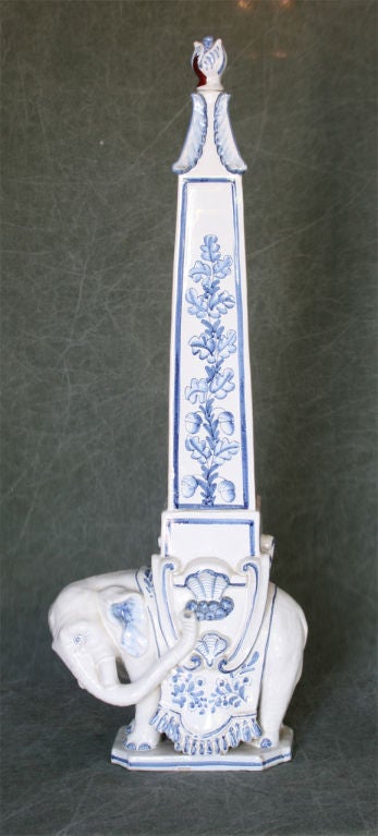 A very charming hand painted glazed ceramic obelisk supported on the back of an elephant. The finial may be easily removed to convert into a lamp.