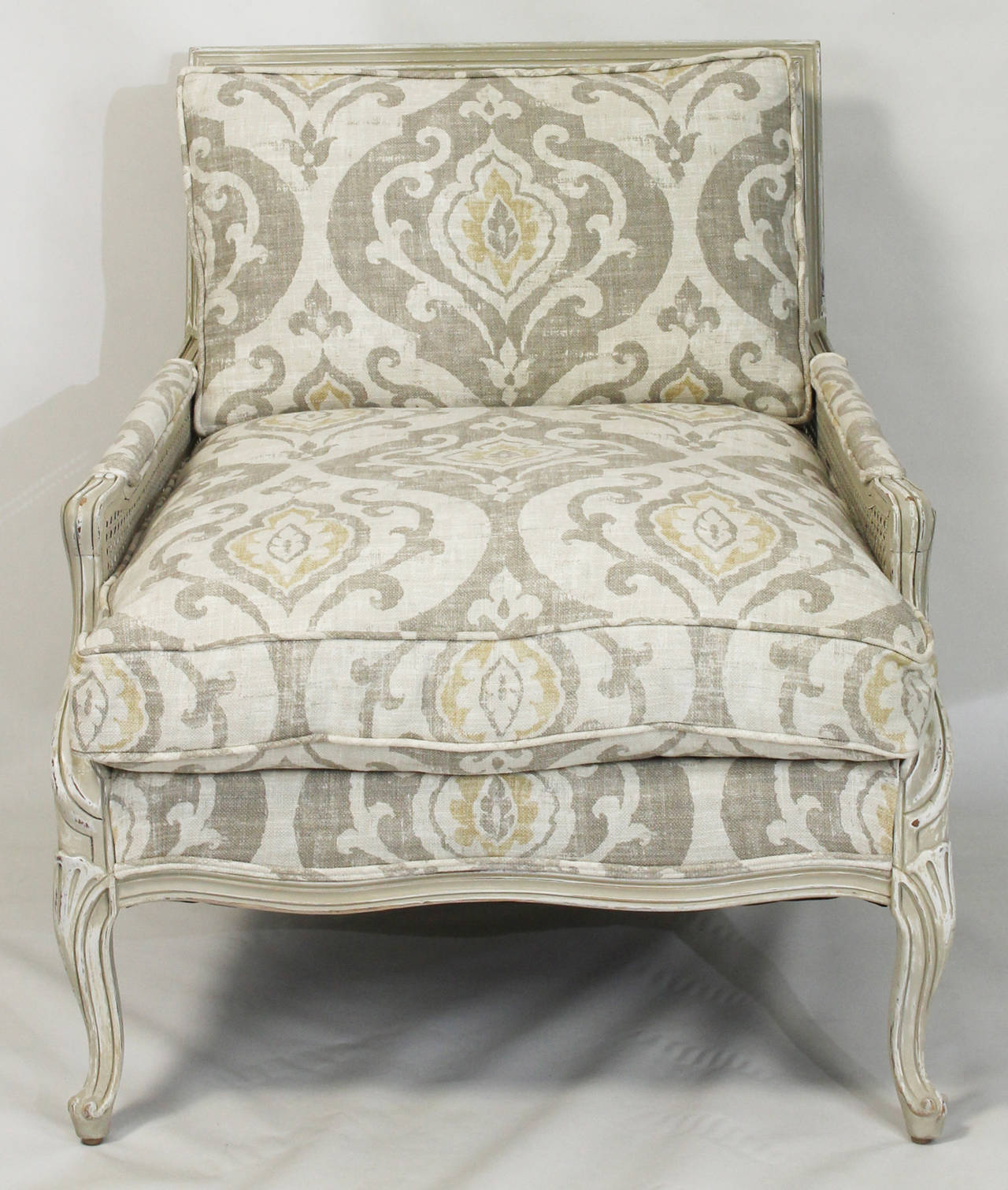 A large French style Bergere dating from the 1940s with cane back and sides in a distressed soft grey paint finish with down seat and back cushions covered in Italian linen fabric.