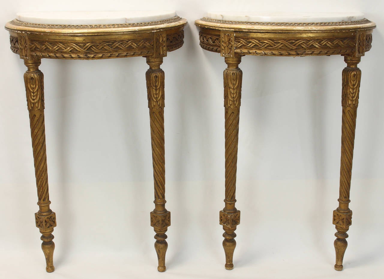 A pair of small late 19th century carved and gilded demilune console tables with white colored marble inset tops.