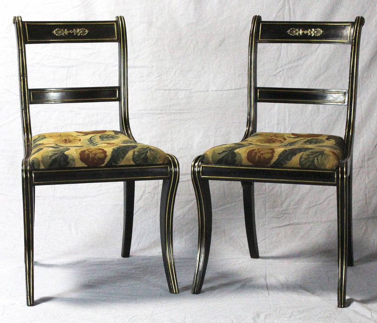 An exceptional set of four English Regency dining chairs dating from the early 19th century. The ebonized chairs are heavily accented with applied brass details. The seats are covered in an old and well done needlepoint fabric.