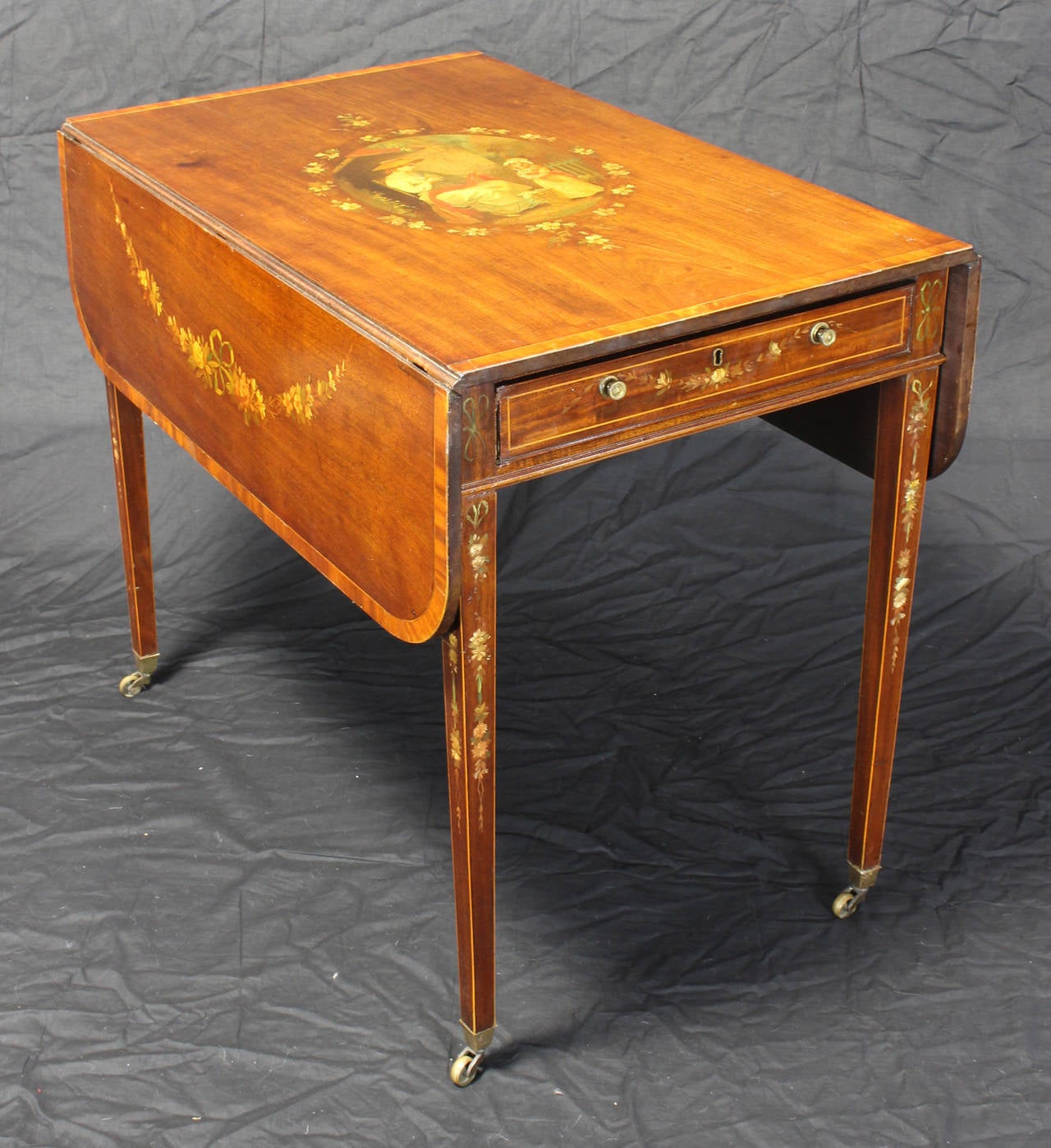 An elegant early 19th century mahogany pembroke table with extensive polychrome decoration on top, drawer and supports. The square tapering legs terminate in original brass casters.
