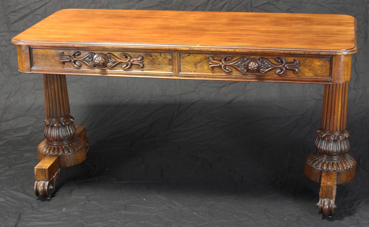 A handsome late Regency or William IV rosewood library table with a pair of frieze drawers and opposing dummies on leaf-clasped supports and sled bases, with carved school toes and casters.