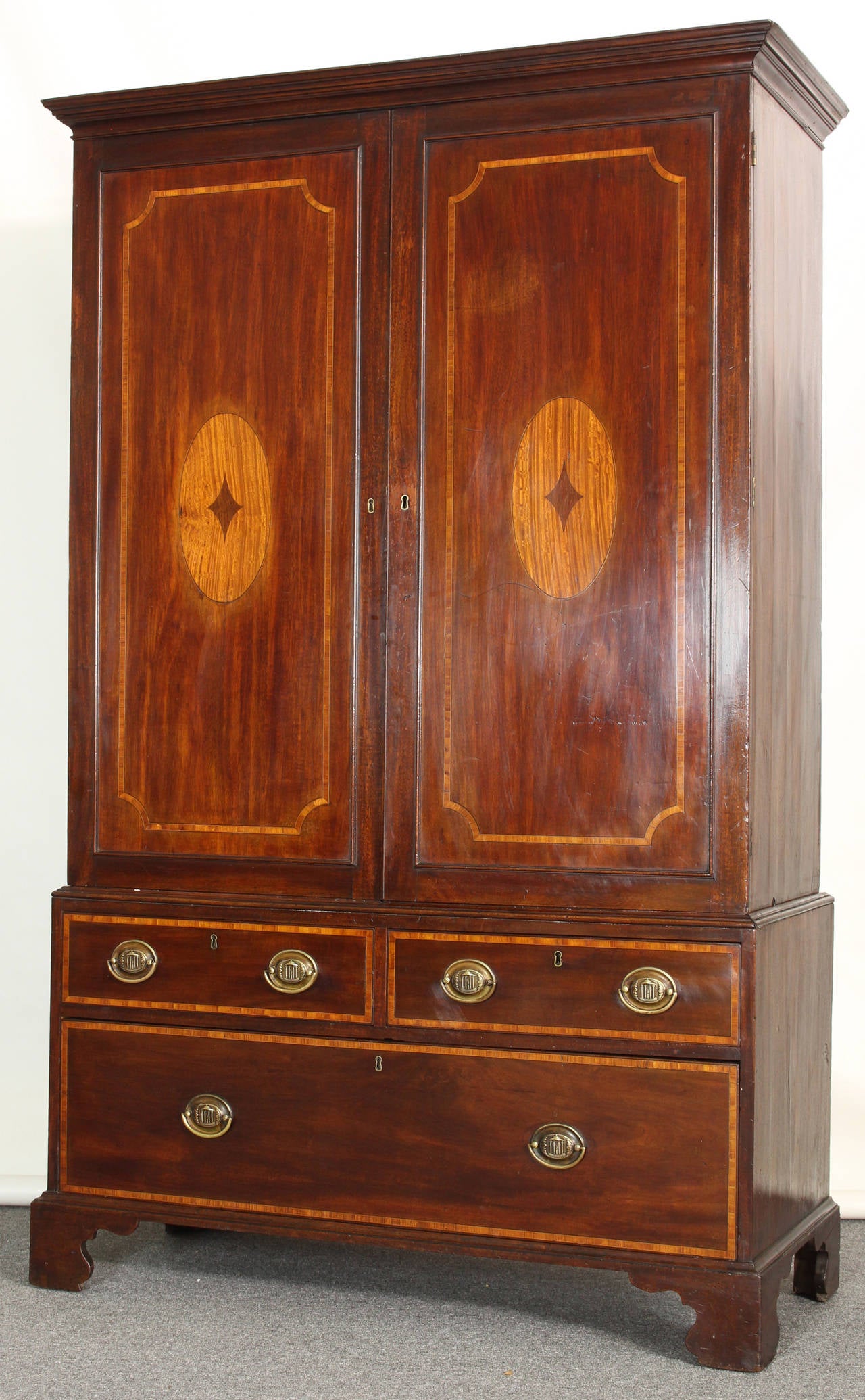 A 19th century English mahogany linen press, with double doors above two short and one long drawer accented with satinwood inlay and original elegant brass pulls, raised on bracket feet.