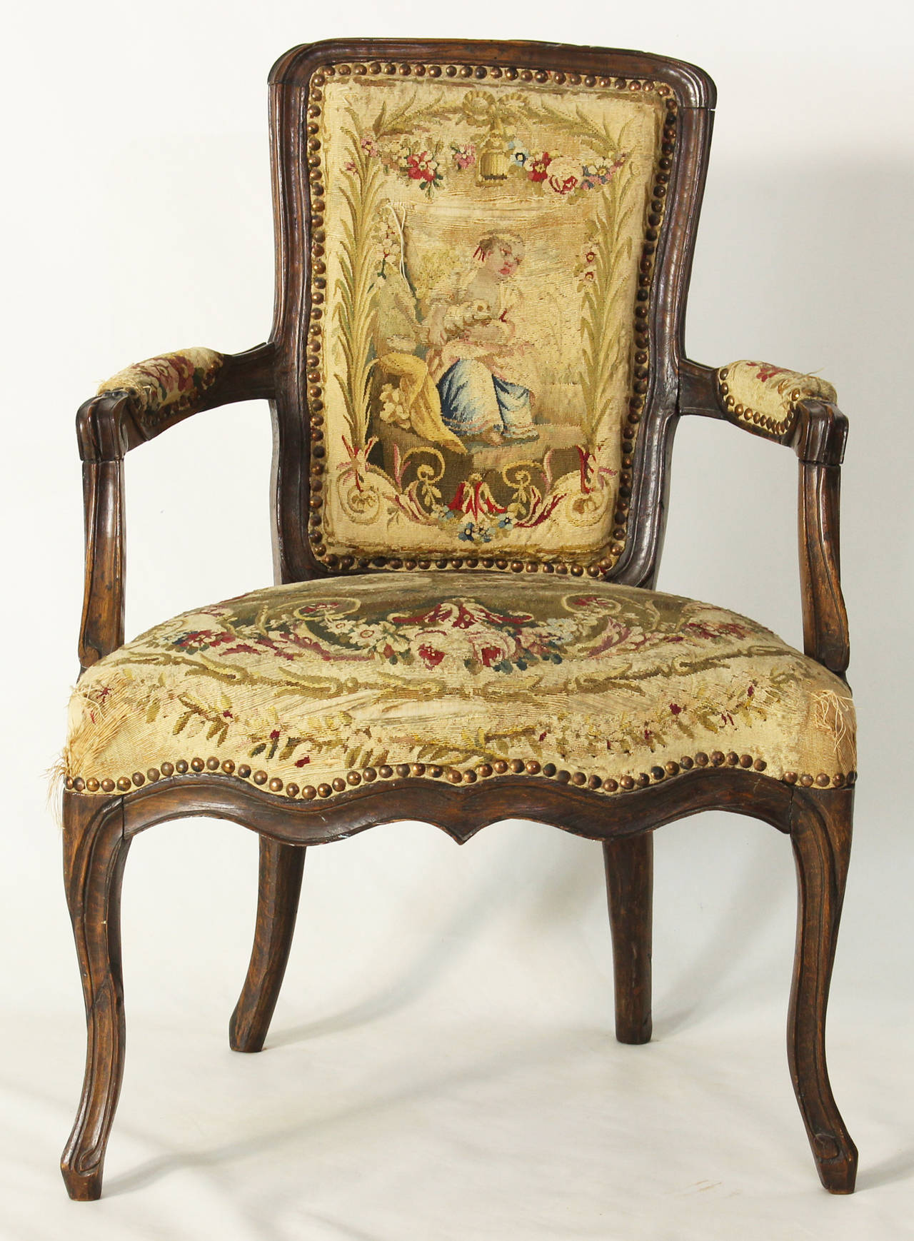 A charming late 18th century French provincial fauteuil retaining its original needlework upholstery and accented with brass nailheads.