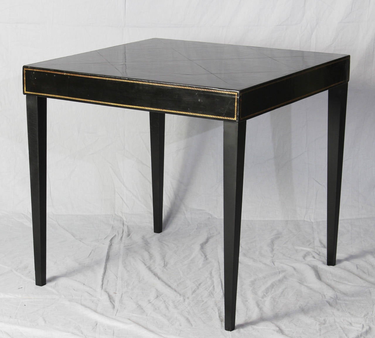 An elegant early 1940's card or game table with tooled leather top and sides on tapering square black lacquer legs