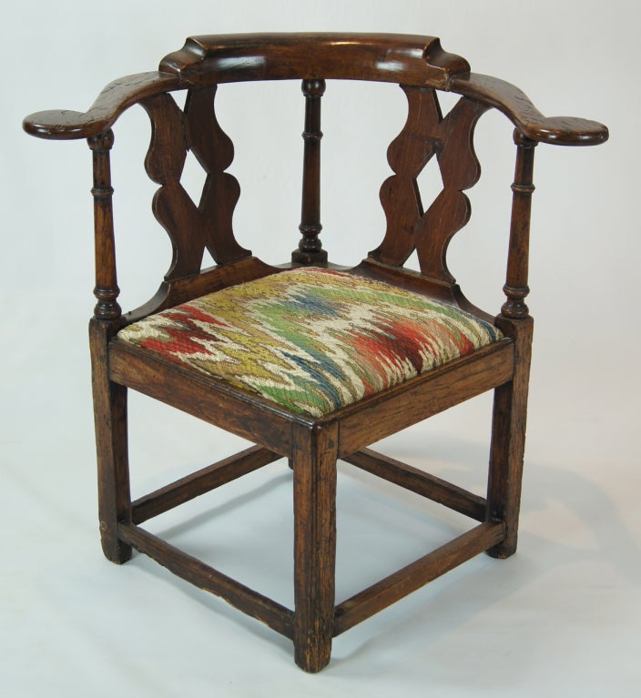 A charming Welsh period oak corner chair of typical smaller size. The dark oak is rich in wear and patina. The seat is drop-in and covered in a vintage flame-stitch fabric in remarkably good condition.