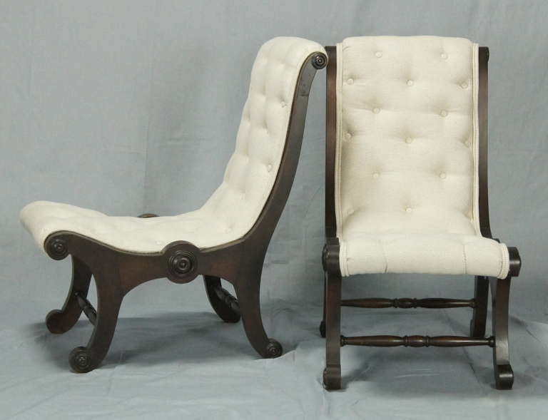 A delightful pair of buttoned Regency style slipper or fireside chairs with carved mahogany frames newly upholstered in a soft grey linen fabric.