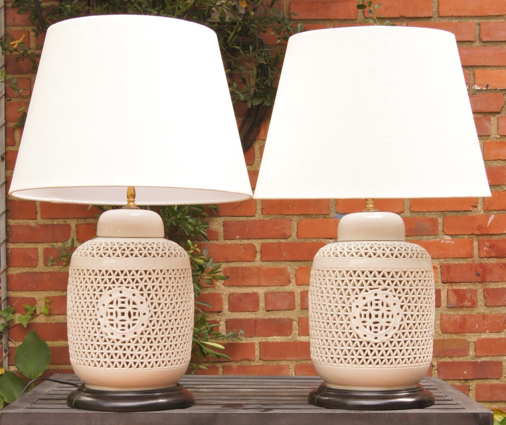 A beautifully scaled pair of 19th C. Blanc de Chine pierced covered jars fashioned into lamps on turned ebonized wood bases.