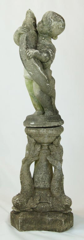 A beautifully weathered cast stone fountain in the form of a boy holding a stylized fish resting on base in the form of three dolphins.