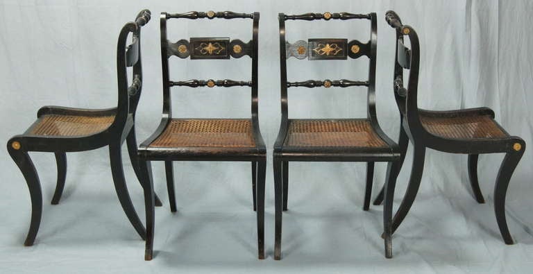 A set of four early 19th century English Regency dining chairs with cane seats, old and possibly original black finish with brass mounts and old gilt decoration.