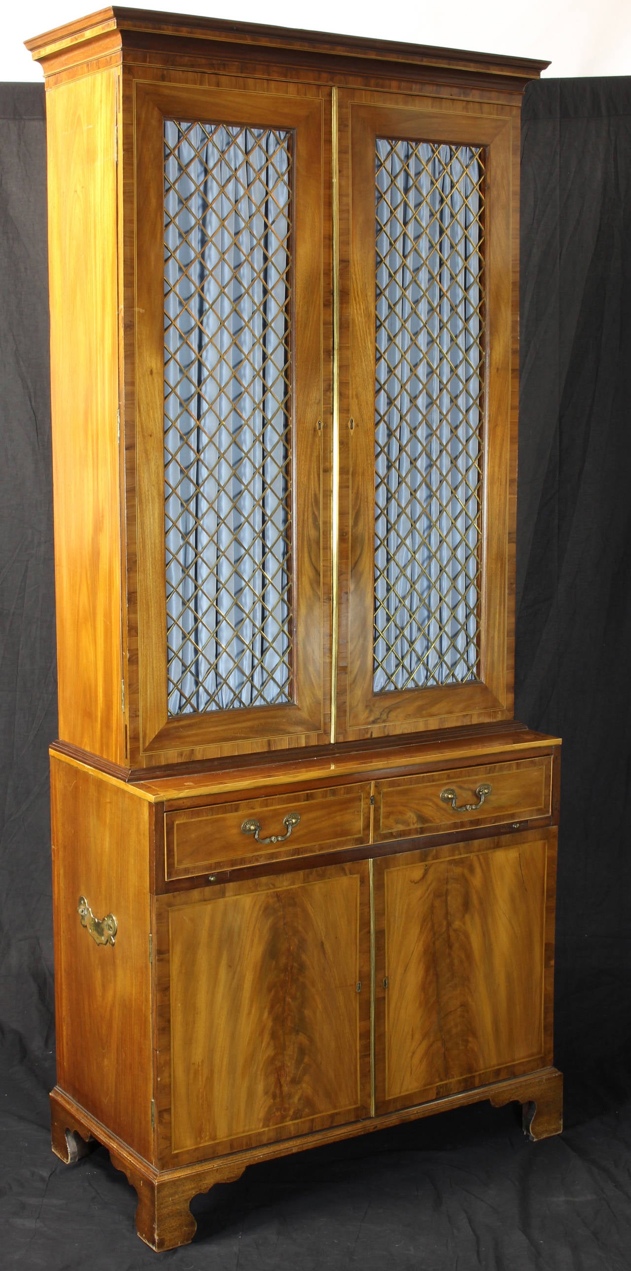 An extremely elegant and beautifully proportioned secretary bookcase made of sun faded mahogany with satinwood accents. The doors are set with diamond shaped grillwork and brass reeding, the lower portion offers a drawer fitted with     a desk above