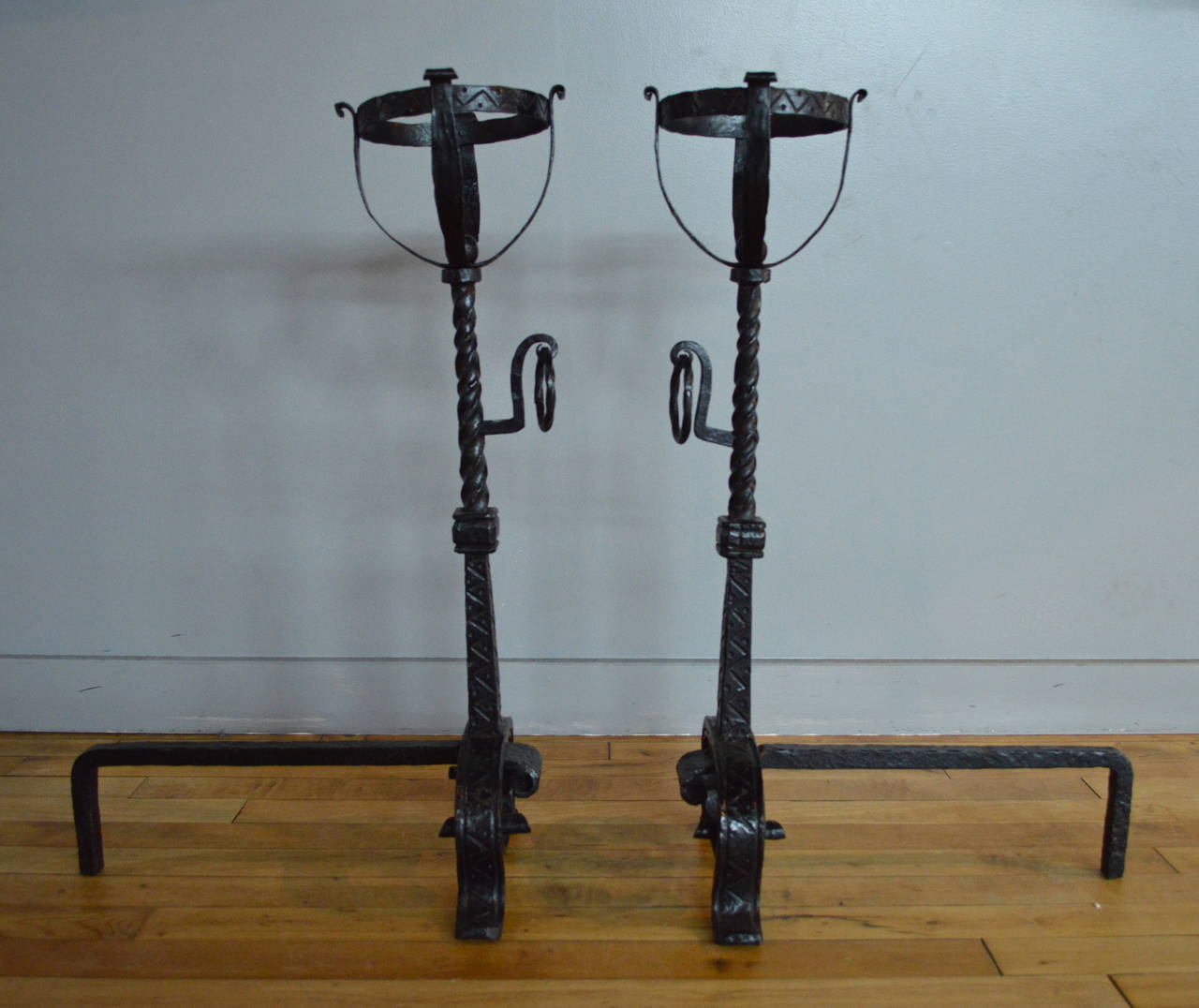 Pair of American late 19th century finely wrought iron andirons with arched scrolled base, incised geometric decorated tapered column with twisted section and hanging ring, surmounted by a basket with incised geometric decorated rim.