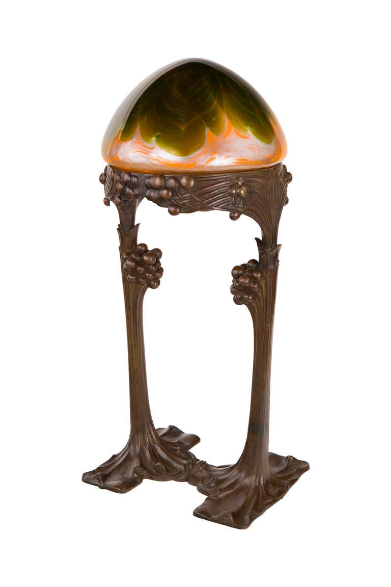 An Austrian Secession patinated bronze and glass table lamp by, Gustav Gurschner decorated with a green pulled feather  against orange background with silver highlights 