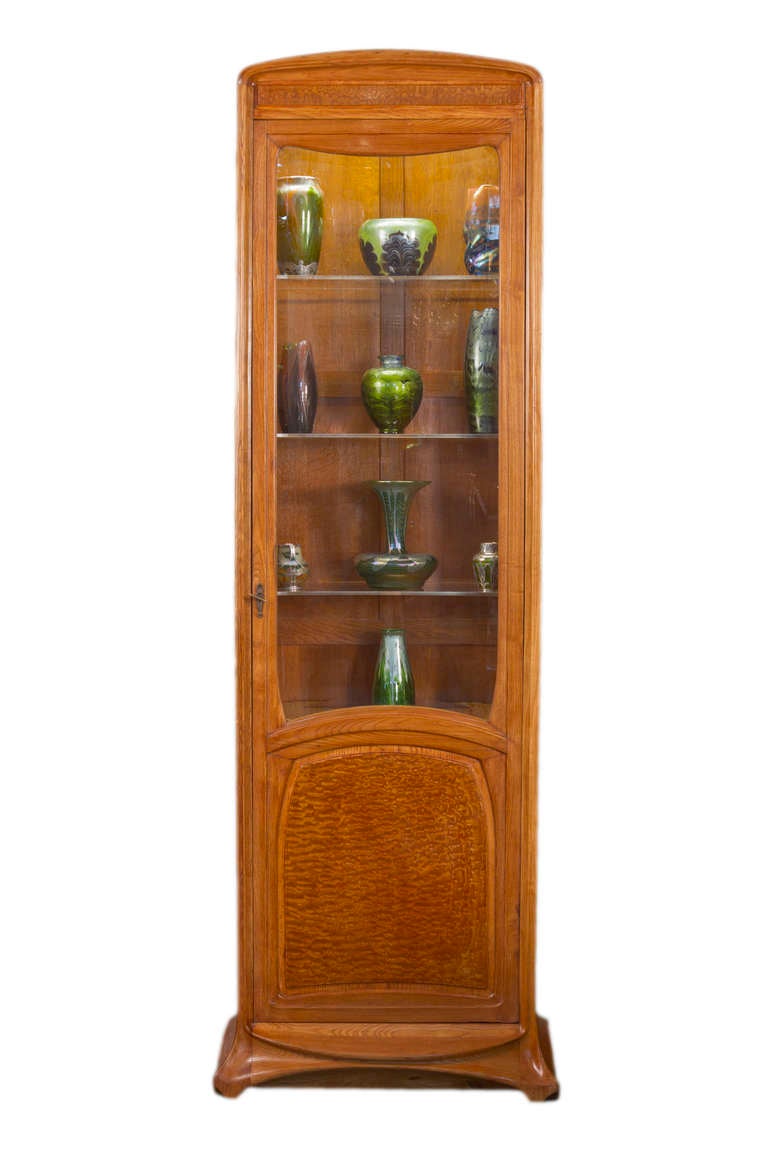A fabulous pair of French Art Nouveau carved walnut and burl wood display cabinets by, Louis Majorelle each carved in classic art nouveau design and with adjustable white glass shelves and a drawer on the interior. The cabinets are illuminated on