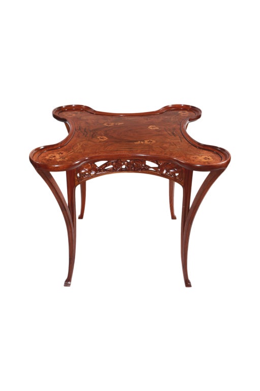 A French Art Nouveau carved mahogany games table by, Camille Gauthier with an exotic fruitwood inlaid marquetry top depicting nasturtium blossoms amongst leaf and vine and the skirt is pierce-carved with nasturtiums. 

Provenance: 
John & Katsy