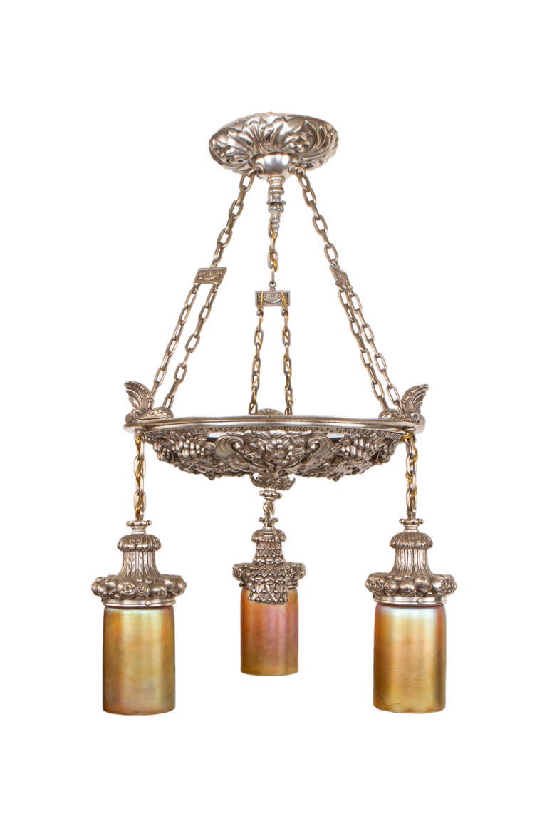 An impressive Late 19th Century American silvered bronze chandelier by, Edward F. Caldwell and Company decorated with pierced bronze figural center plate of three classical faces amongst poppy flowers further decorated with three gold 