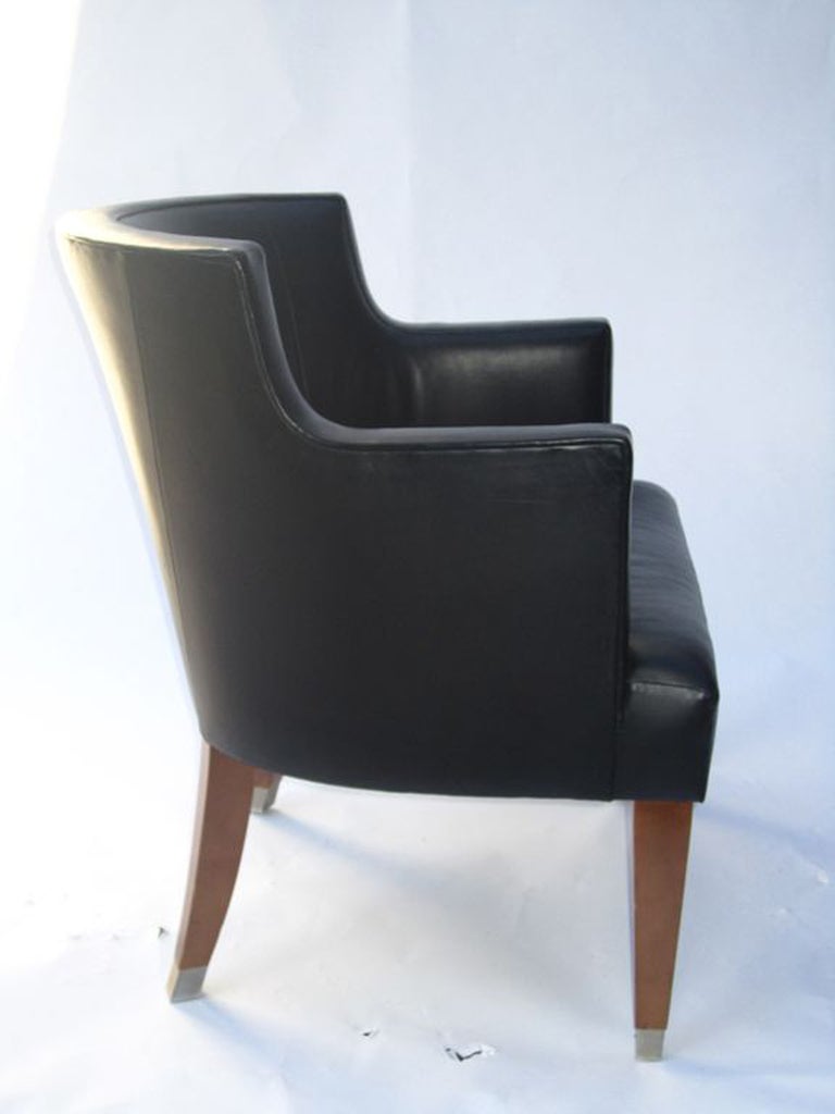 A vintage barrel back armchair in black leather with tapered wooden legs. The piece retains its HBF manufacturer label on the bottom.