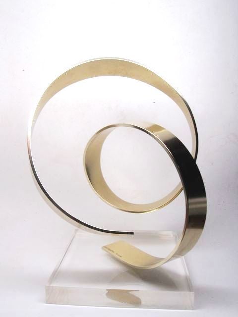 A vintage brass swirl form kinetic sculpture on a clear lucite base. The piece is signed and dated by the artist (Dan Murphy 1978).