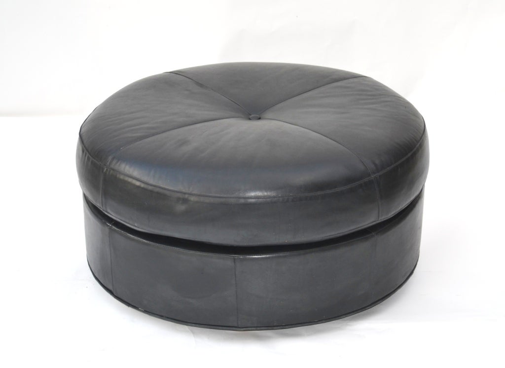 A custom made round ottoman or stool on casters with a button tuft detail. The piece has been upholstered in black coach leather.