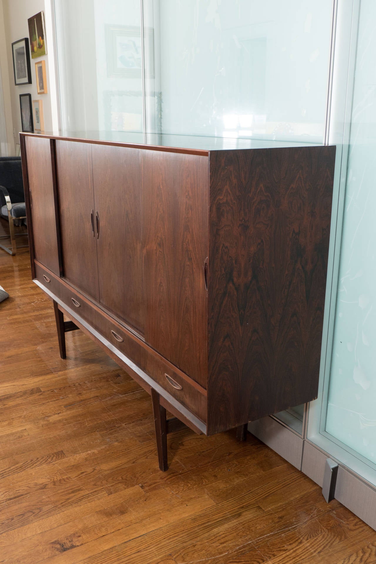 A tall Danish credenza, in the Scandinavian Modern style, with four sliding doors, inset with shelving units, including a mirrored back bar cabinet on the far right side, above four lower drawers, on square tapered legs. Good condition, with age