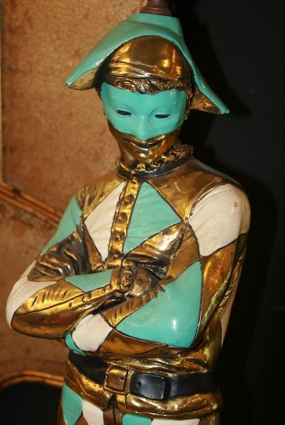 A sinlge enameled bronze table lamp depicting a harlequin in turquise and white costume, on a square black base.