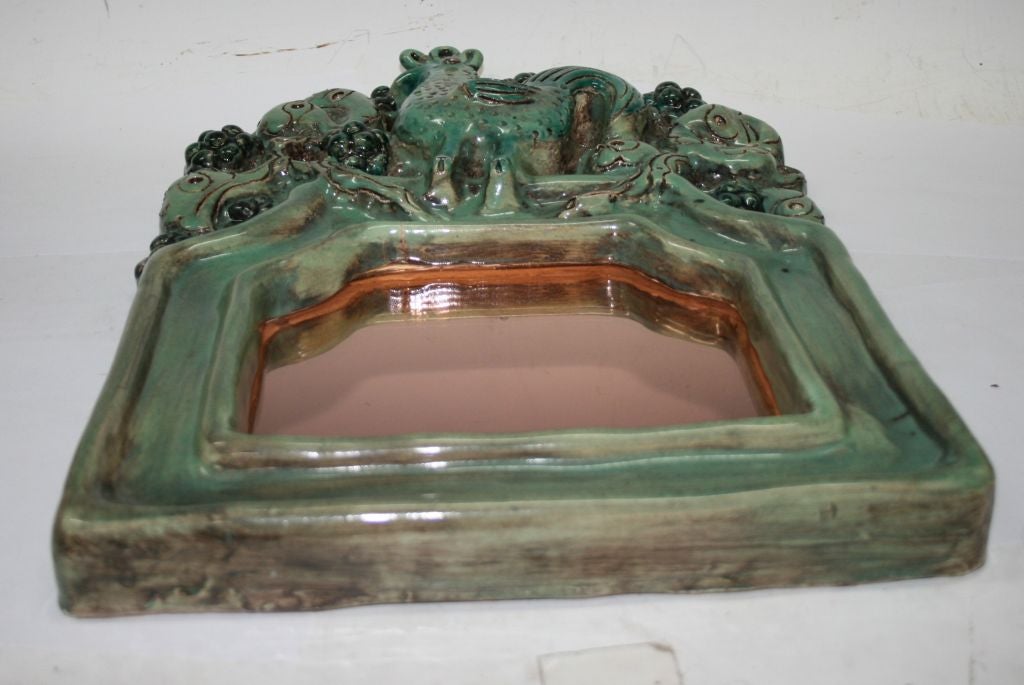 A green glazed ceramic three dimensional mirror frame by Georges Jouve depicting a rooster in front of a stylized berry bush. Signed on the back with the GJ cypher and 