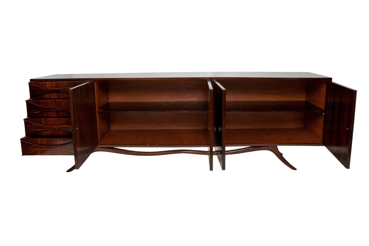 A long buffet and credenza, produced in Brazil, circa 1950s, in lacquered jacaranda wood, with four doors for dual storage spaces, each inset with single shelf, and four adjacent drawers with bow-tie pulls, on beautifully formed curved base with