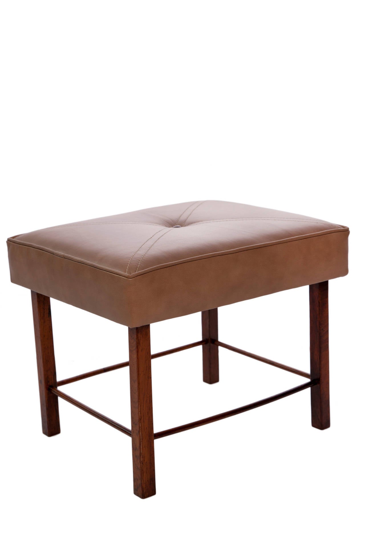 A vintage stool, produced circa 1960s, seat upholstered in tufted beige leather, with single wood button and crossed stitching accents, over a jacaranda wood frame, legs and four cylindrical beam stretchers. Good vintage condition, with age