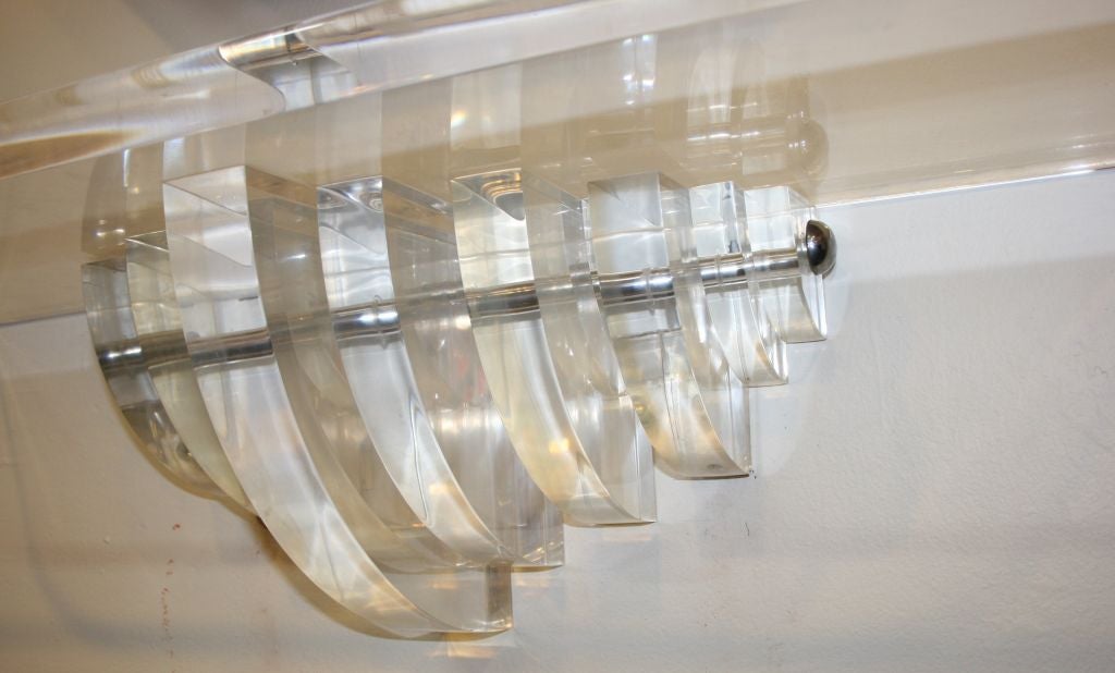 A thick Lucite wall-mounted shelf with stepped bracket and rounded edges. Chrome accents.