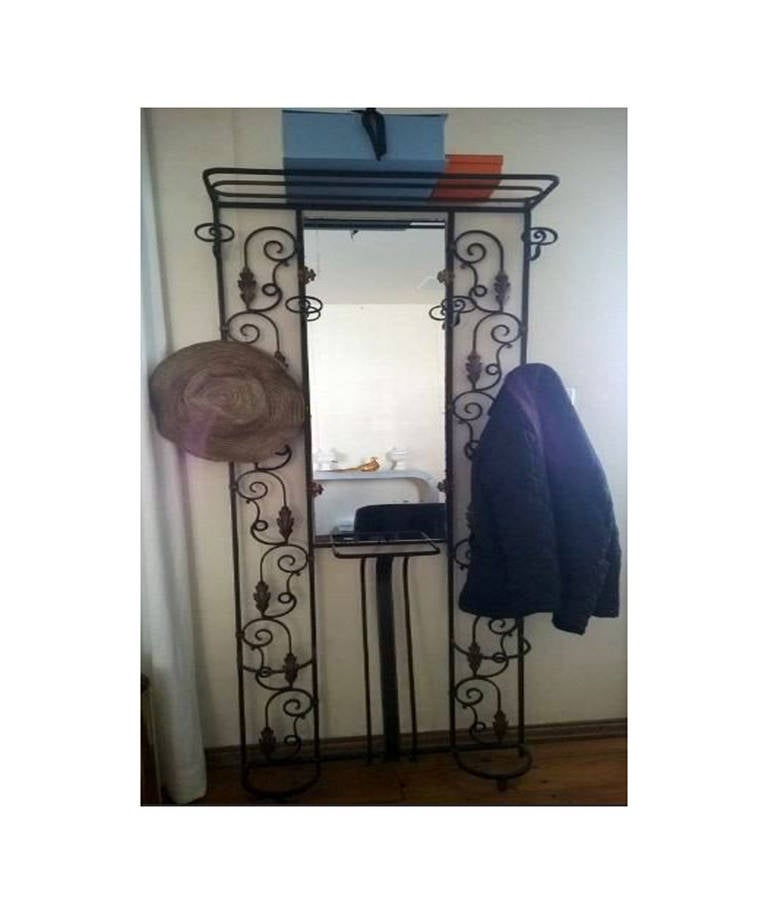 A beautiful and substantial wrought iron black and gold, wall mounted, hall tree or coat rack with mirror. This piece has an swirl design with gold leaf accents. There are six hat or clothing hooks, two umbrella holders, a top shelf/storage area,