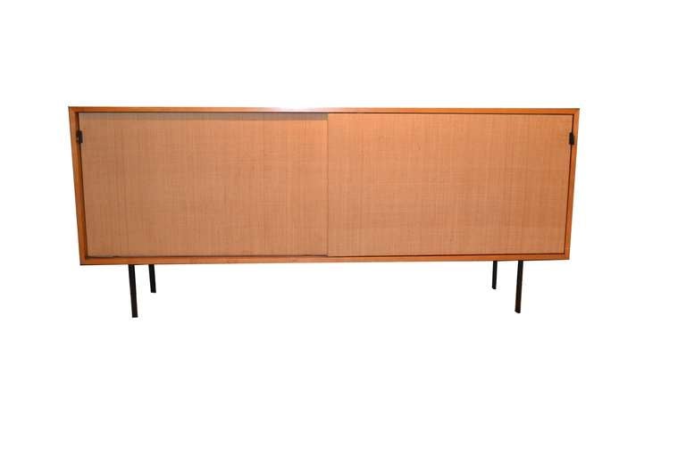 A vintage credenza or sideboard with raffia covered sliding doors and leather pulls. The piece is attributed to Florence Knoll. Vintage condition with wear commensurate with age and use; some loose veneer.