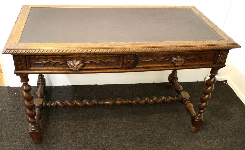A Henri II style chestnut writing desk created in the Loire Valley in France during the first part of the 20th Century has a leather inset writing surface, turned wood legs and stretcher and unique hand carved gargoyle head drawer pulls. Two drawers