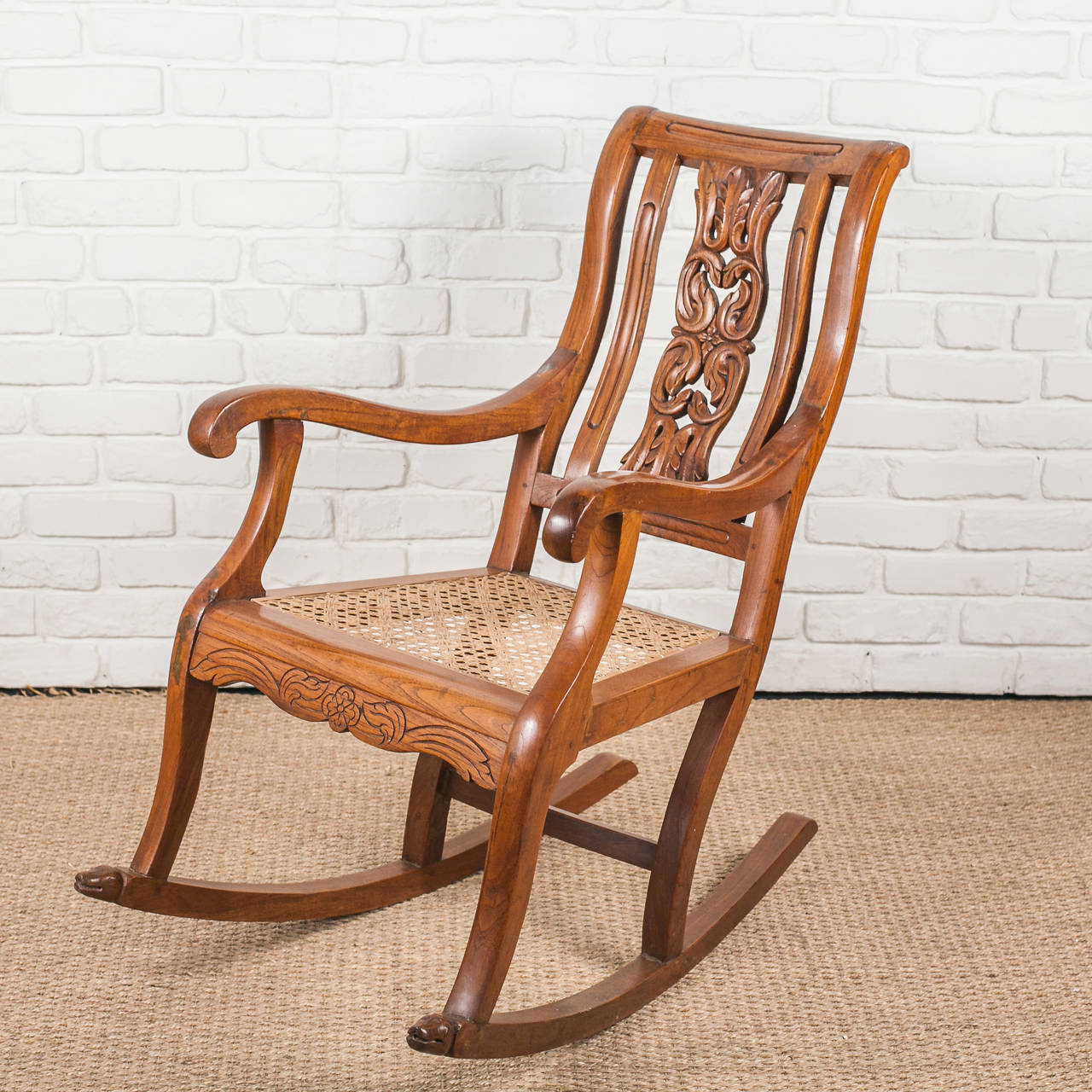 Indo-Portuguese rocking chair in solid teak with carved back and front stretcher. Dog heads carved on front of legs.