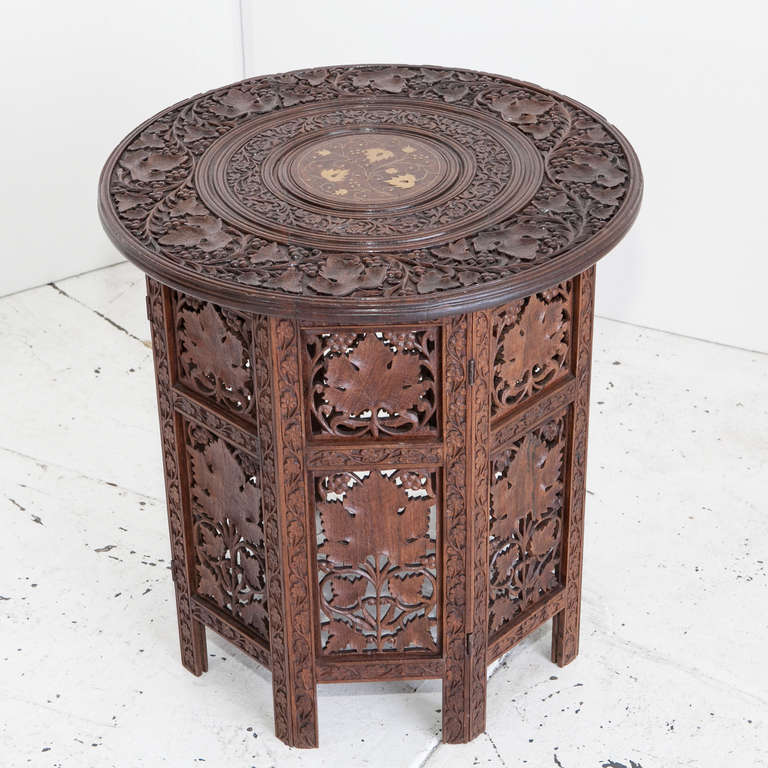 Anglo-Indian rosewood teapoy or side table has elaborately carved leaf designs on base and top. The top has brass inlay in the center. The top and bottom come apart and the base folds flat.