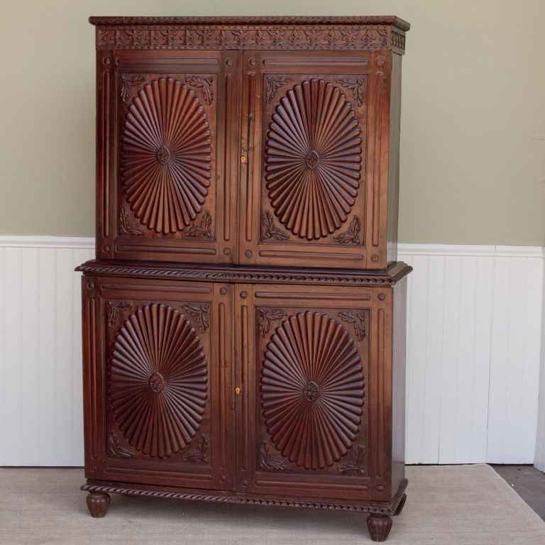 Indo-Portuguese solid rosewood armoire with stylized sunburst pattern carving on doors. Cabinet is in two parts, top cabinet has two removable shelves, bottom cabinet has single removable shelf. Cabinet rests on carved feet.