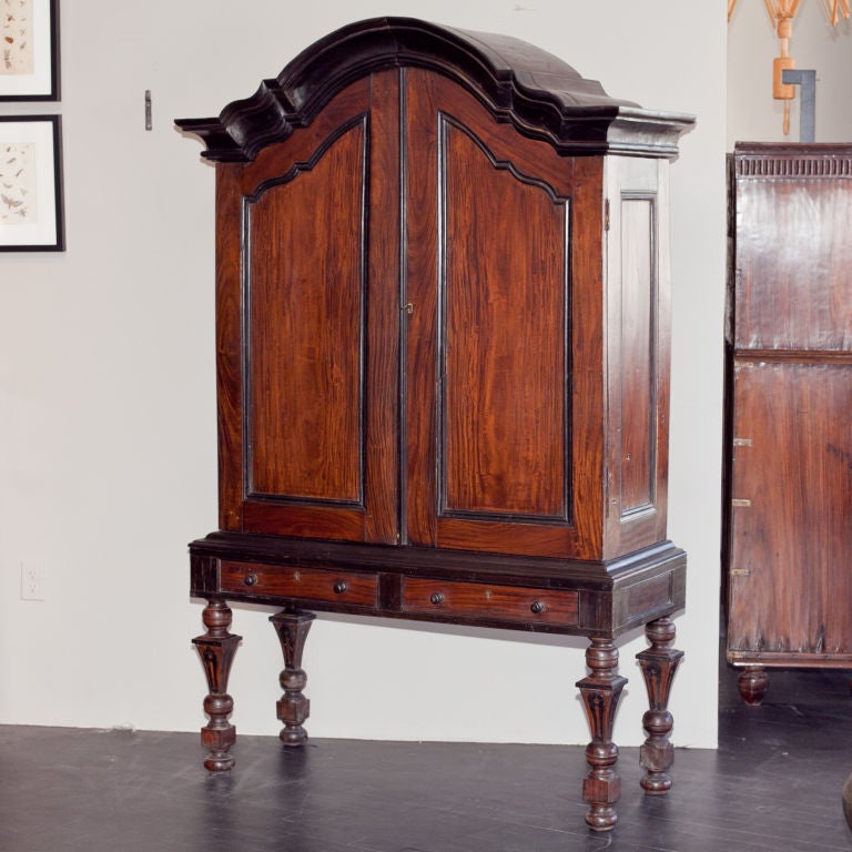 Exceptionally rare Indo-Dutch cabinet made of solid satinwood with ebony trim and inlay. Large gable is carved from solid ebony. Cabinet collapses flat. Base and legs have ebony inlay. Base has two drawers with ebony handles, brass escutcheons and