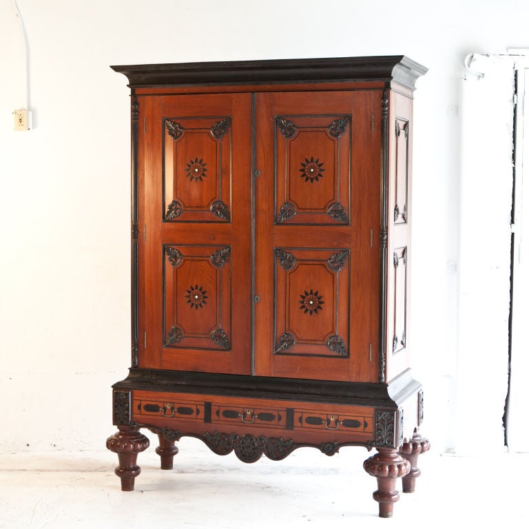 Dutch colonial armoire consisting of two door upper cabinet with ebony detailed raised panel doors, interior has three shelves. Bottom cabinet has three drawers with ebony inlay and brass handles.