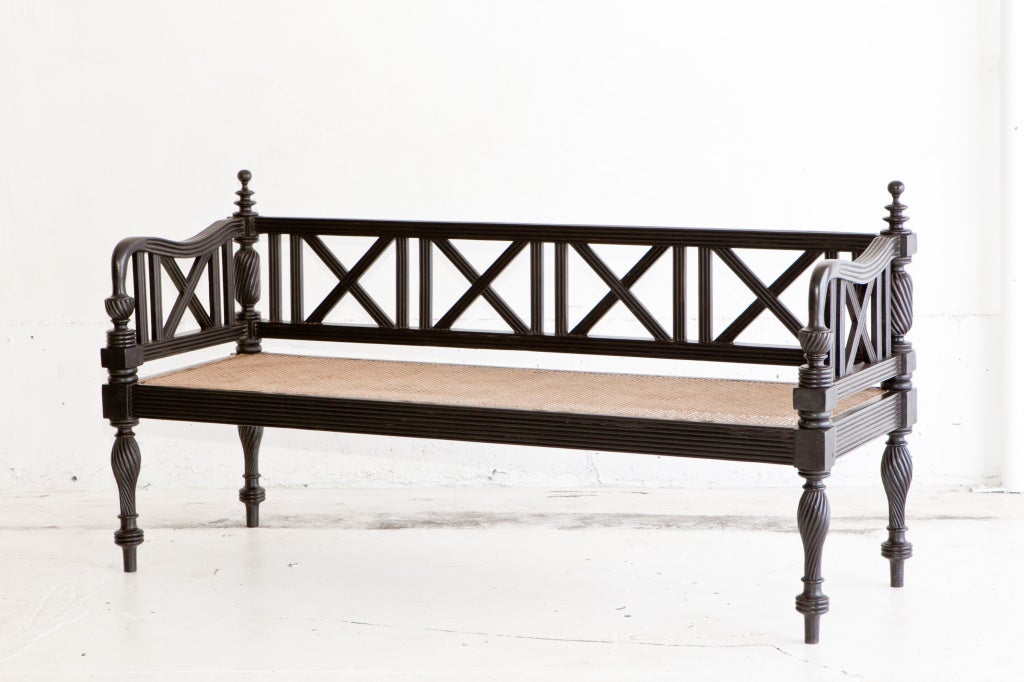 A solid ebony caned bench with deep flute carving on almost every flat surface. Turned finials sit a top rear posts with fluted carving. Rear splats and side splats have fluted surface on both sides. Turned front legs also have fluting and end in