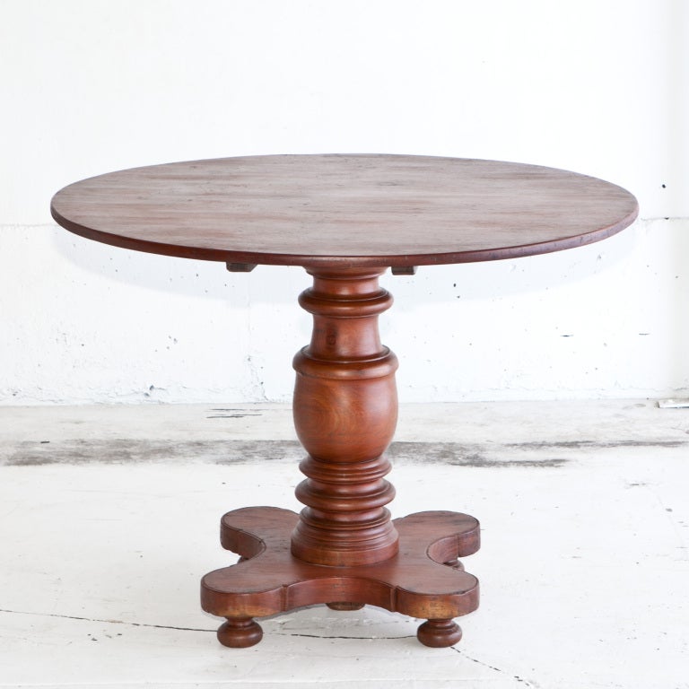 Round tilt top table made of jackfruit wood. Carved wood base that rests on four feet.
