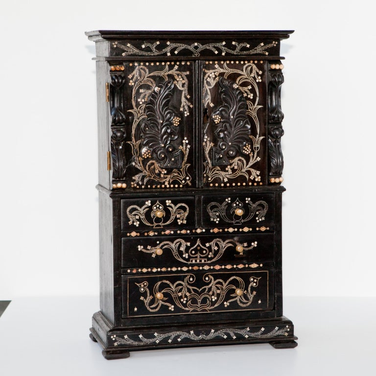 Anglo-Indian miniature cabinet made of solid ebony with ivory inlay and additional ebony carved details. Features 2 over 2 drawers with ivory pulls and a top two door cabinet.